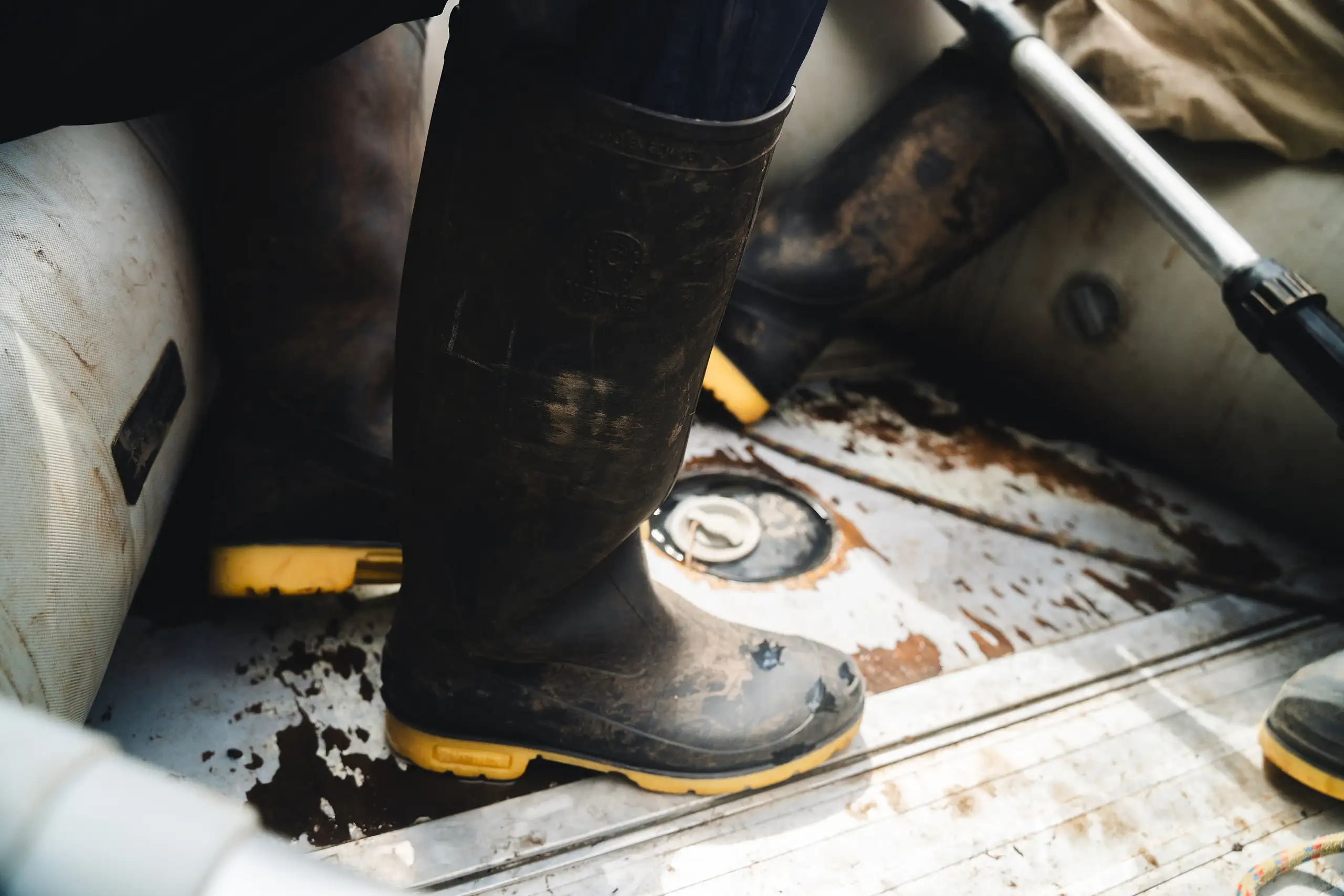 Close-up of mud-caked rubber boots with yellow soles on the floor of an inflatable boat, an oar resting against the side, Laguna de los Cóndores, Amazonas, Peru