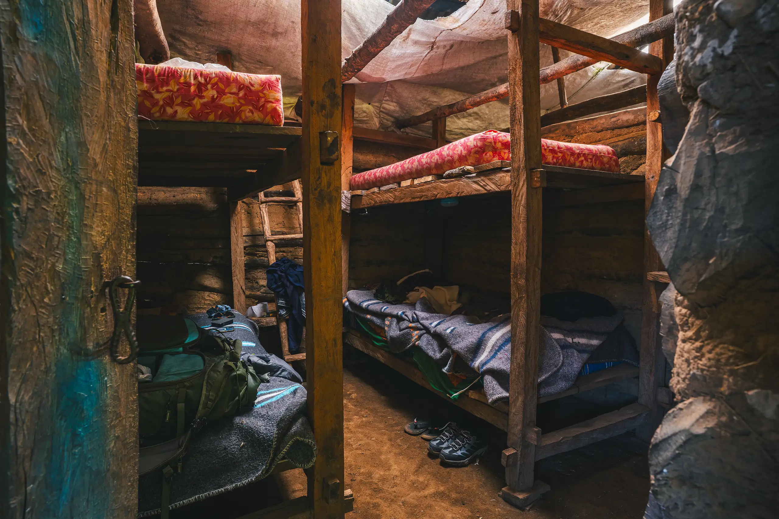 Rough wooden bunk beds with bright red mattresses and wool blankets in a dim room, backpacks and boots on the earth floor, Laguna de los Cóndores, Amazonas, Peru