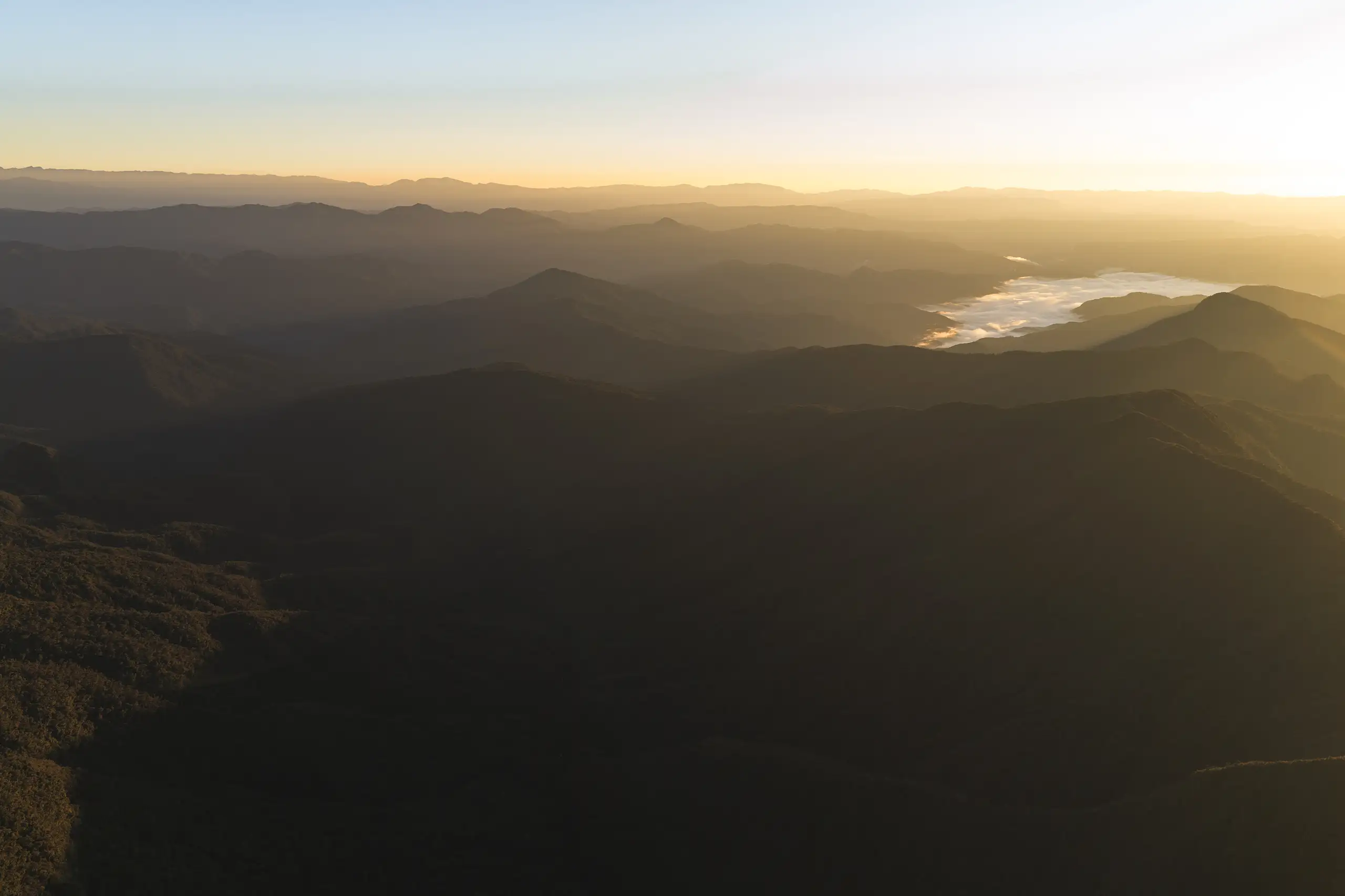Layer upon layer of dark forested ridges under a golden sky, a sea of cloud filling a distant valley, Laguna de los Cóndores, Amazonas, Peru