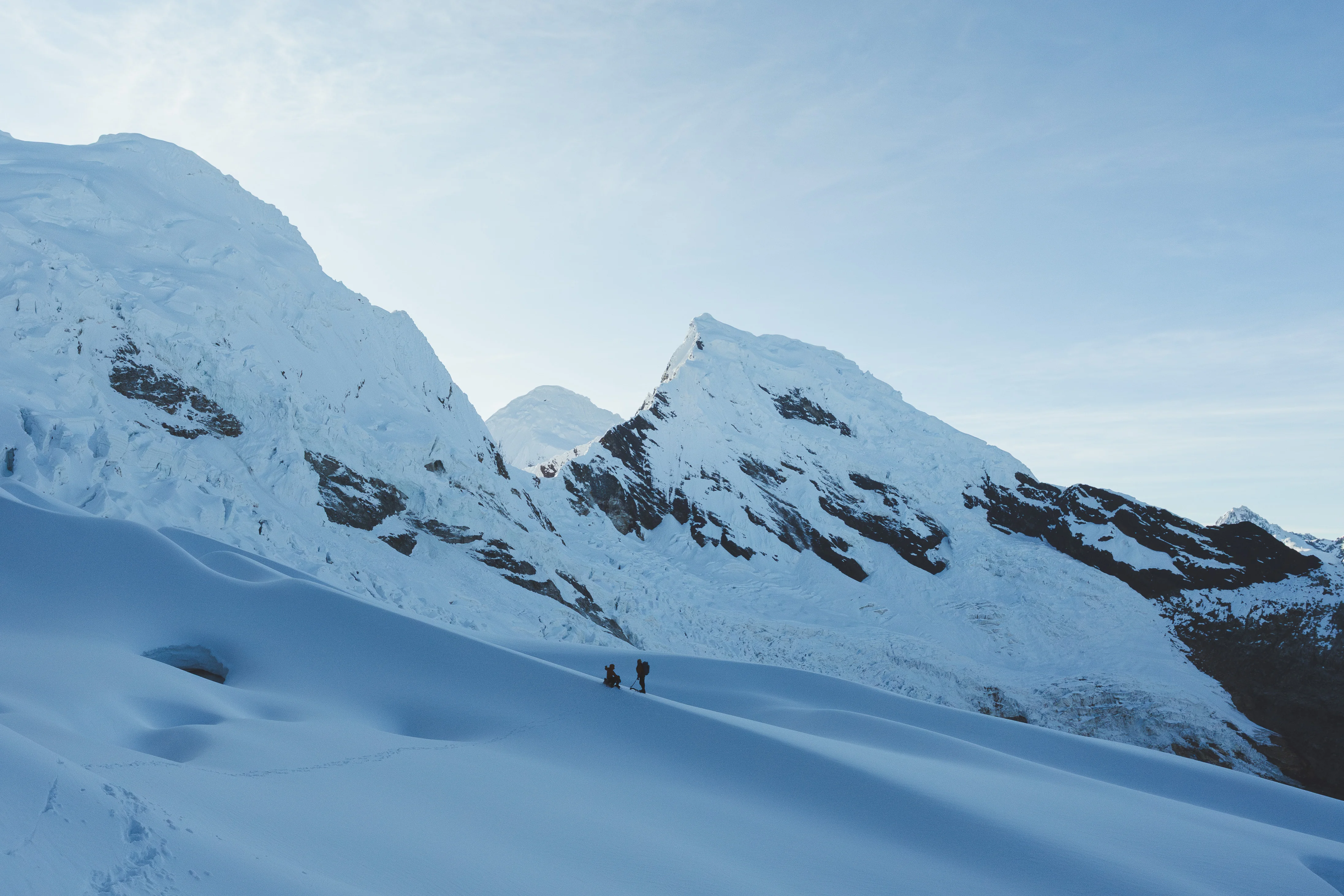 Two climbers reduced to specks on a wide snow slope beneath the huge walls of Nevado Palcaraju West, Pucaranra and Chinchey beyond, Cordillera Blanca, Peru