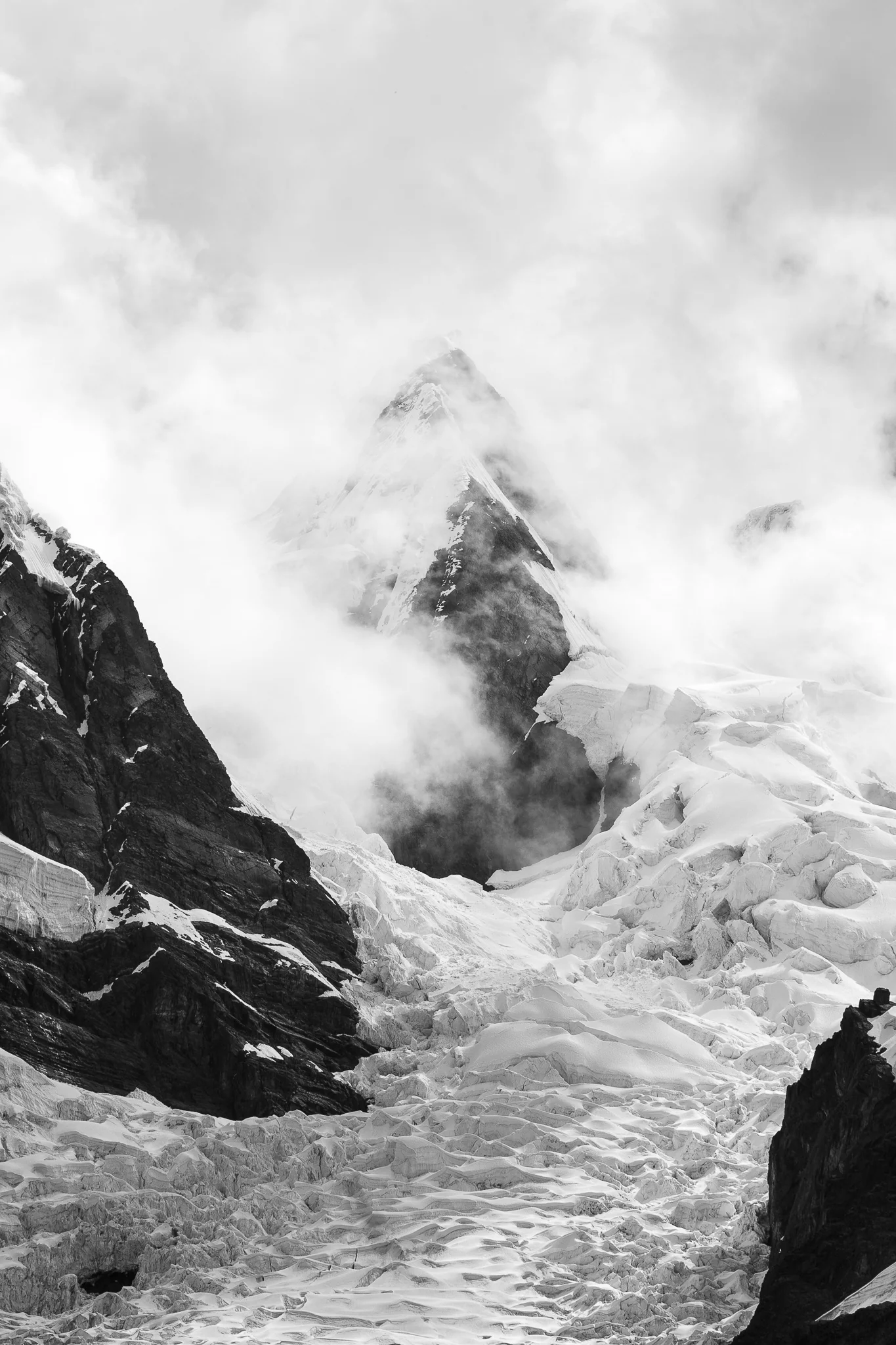Black-and-white view of a broken glacier tumbling between dark rock walls, the summit of Nevados Pucajirca lost in cloud above, Cordillera Blanca, Peru