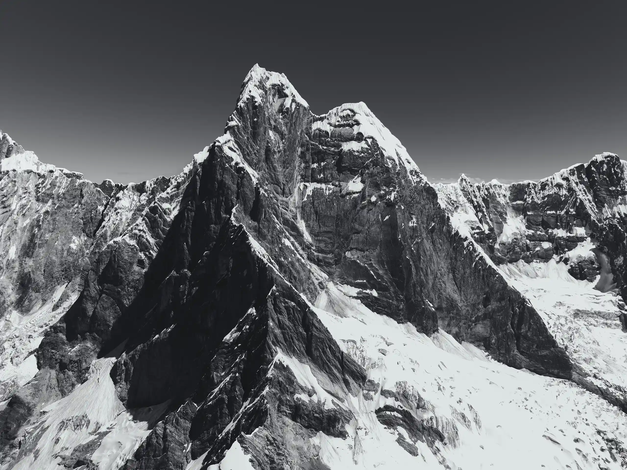Black-and-white aerial view of the steep rock and ice face of Nevado Jirishanca from the summit of Jirishanca Chico, Cordillera Huayhuash, Peru