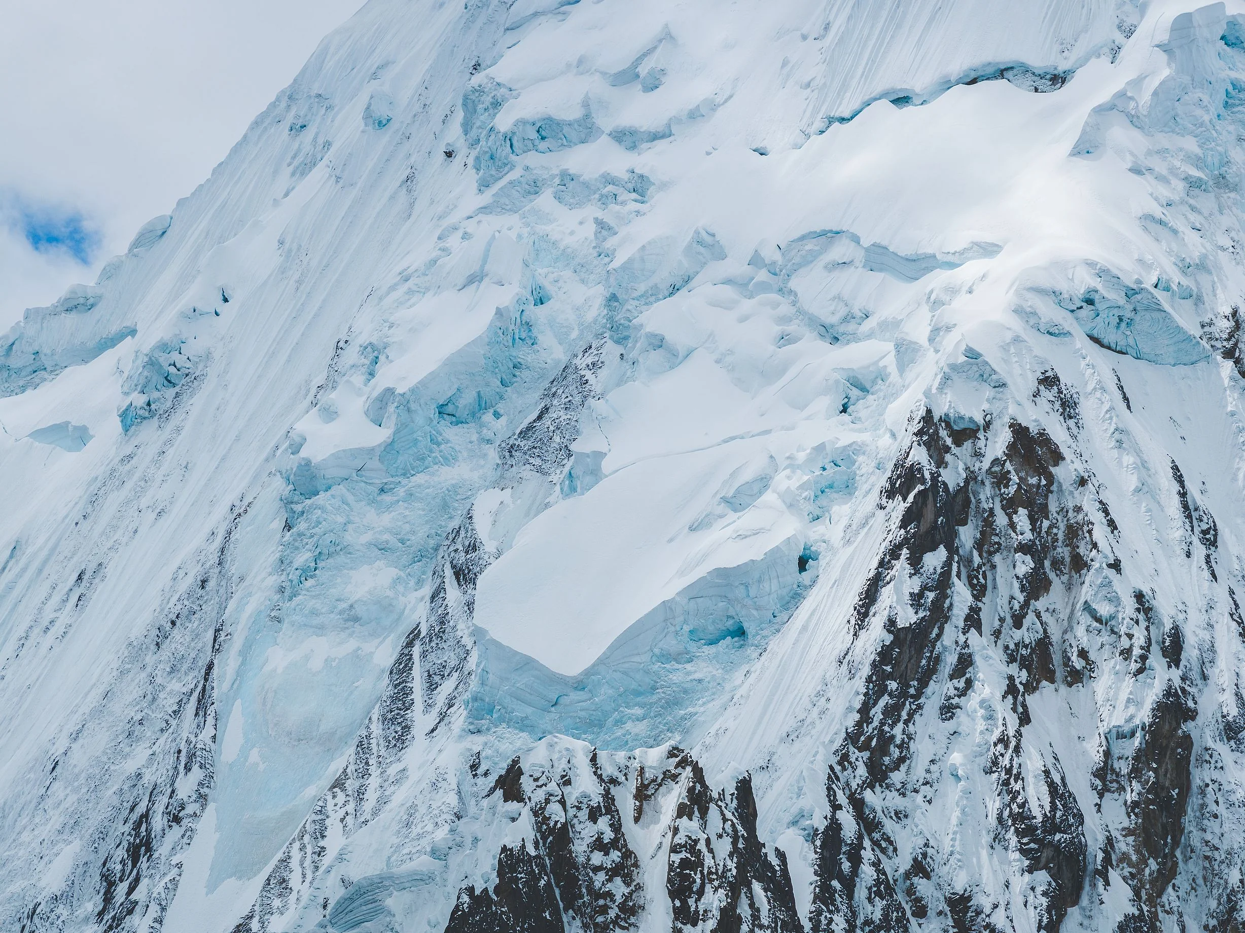 Close view of a glacier with blue ice cliffs and seracs spilling over dark rock, Cordillera Huayhuash, Peru