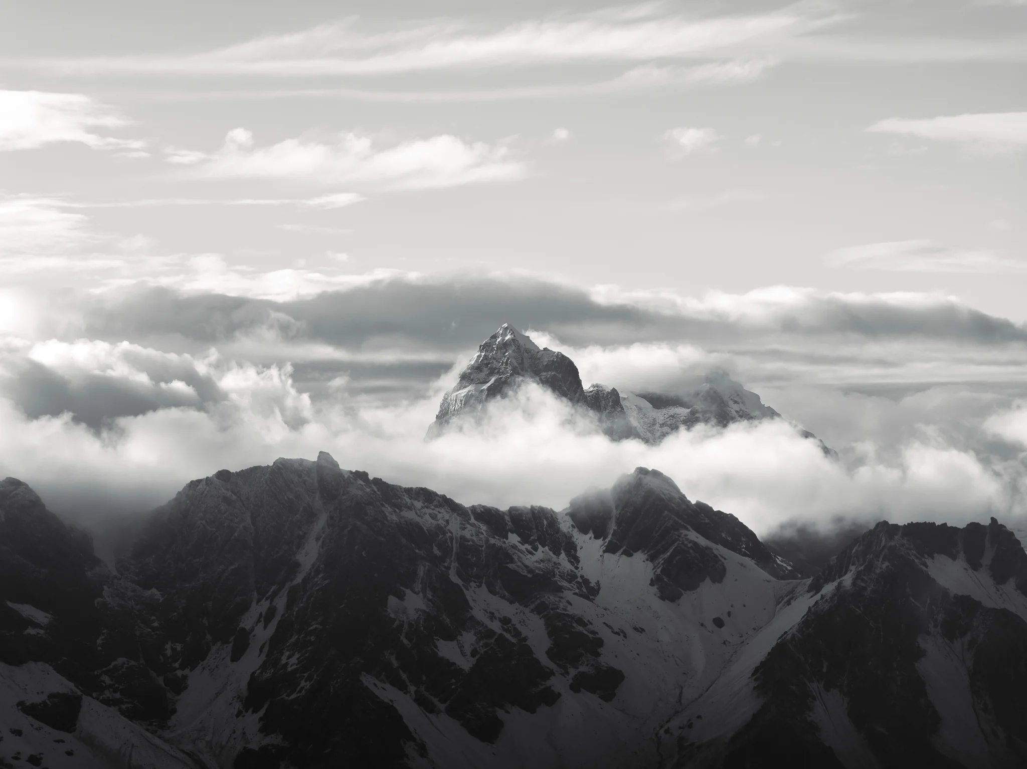 Black-and-white aerial view of the rocky summit of Nevado Puscanturpa standing above a bank of cloud, Cordillera Huayhuash, Peru