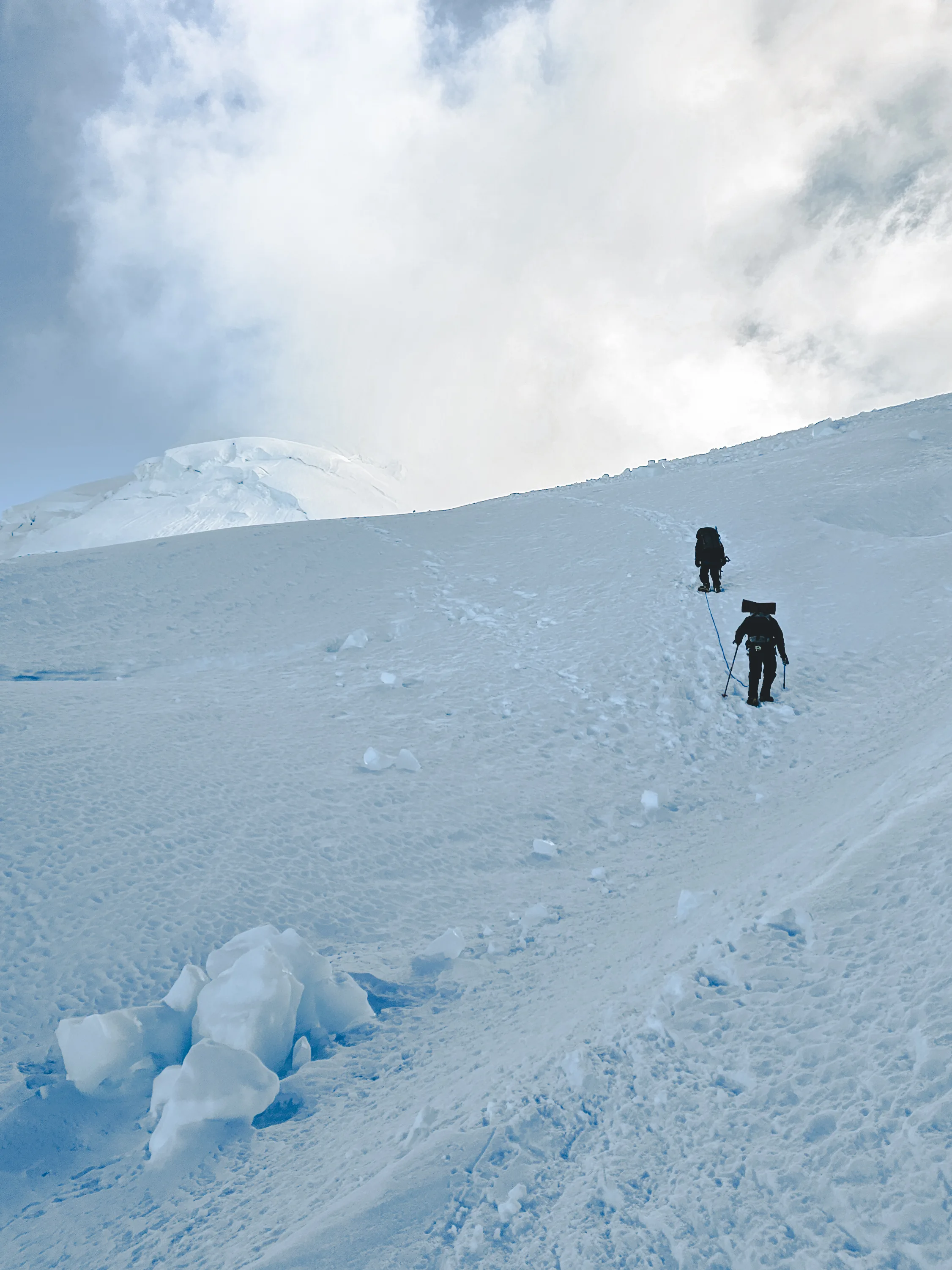 Vertical view of two climbers far up a long, steep snow slope on Nevado Huascarán, heading into the clouds, Cordillera Blanca, Peru