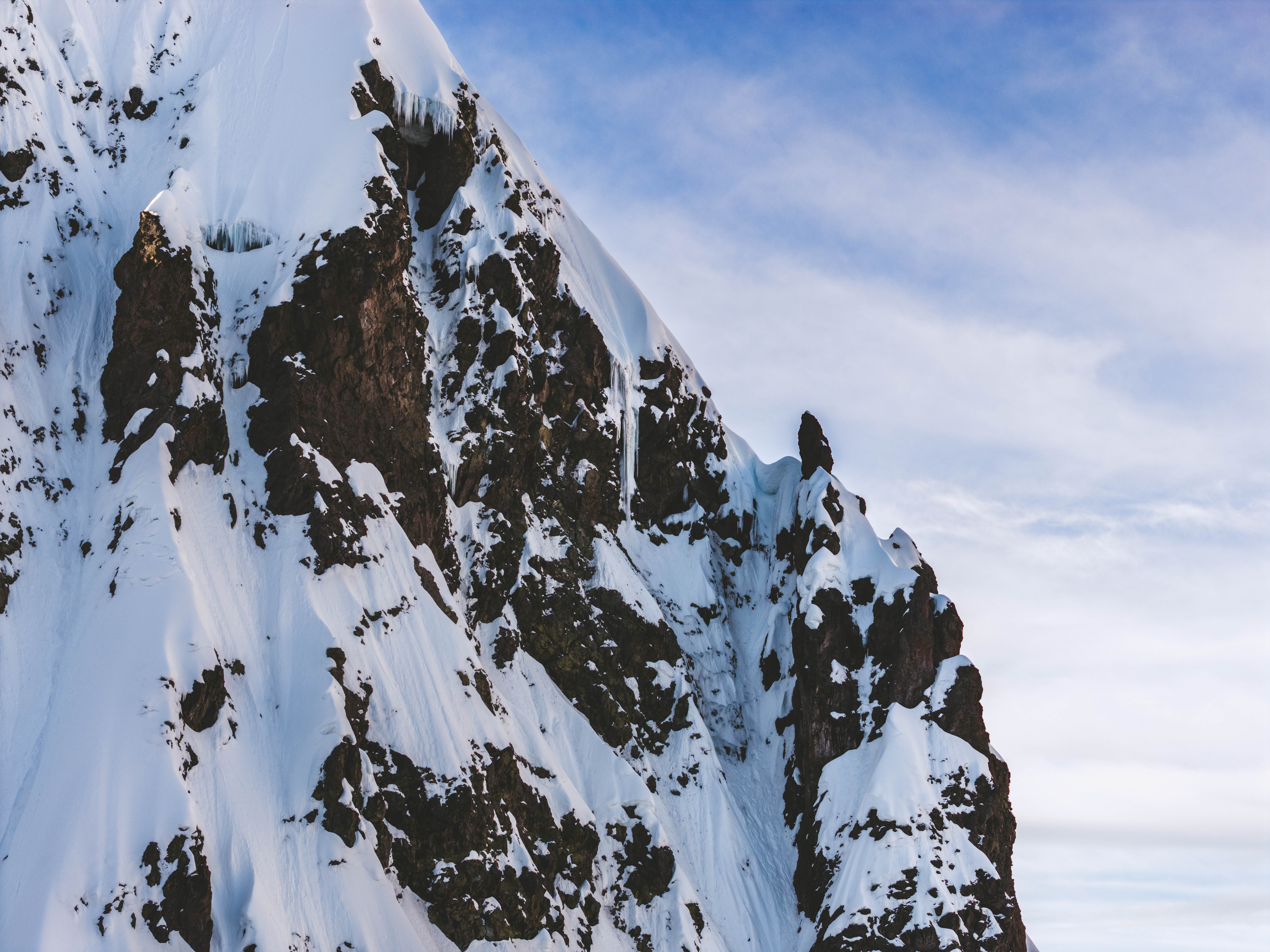 A steep buttress of dark rock plastered with snow and ice, its crest cutting across a pale sky, Peru