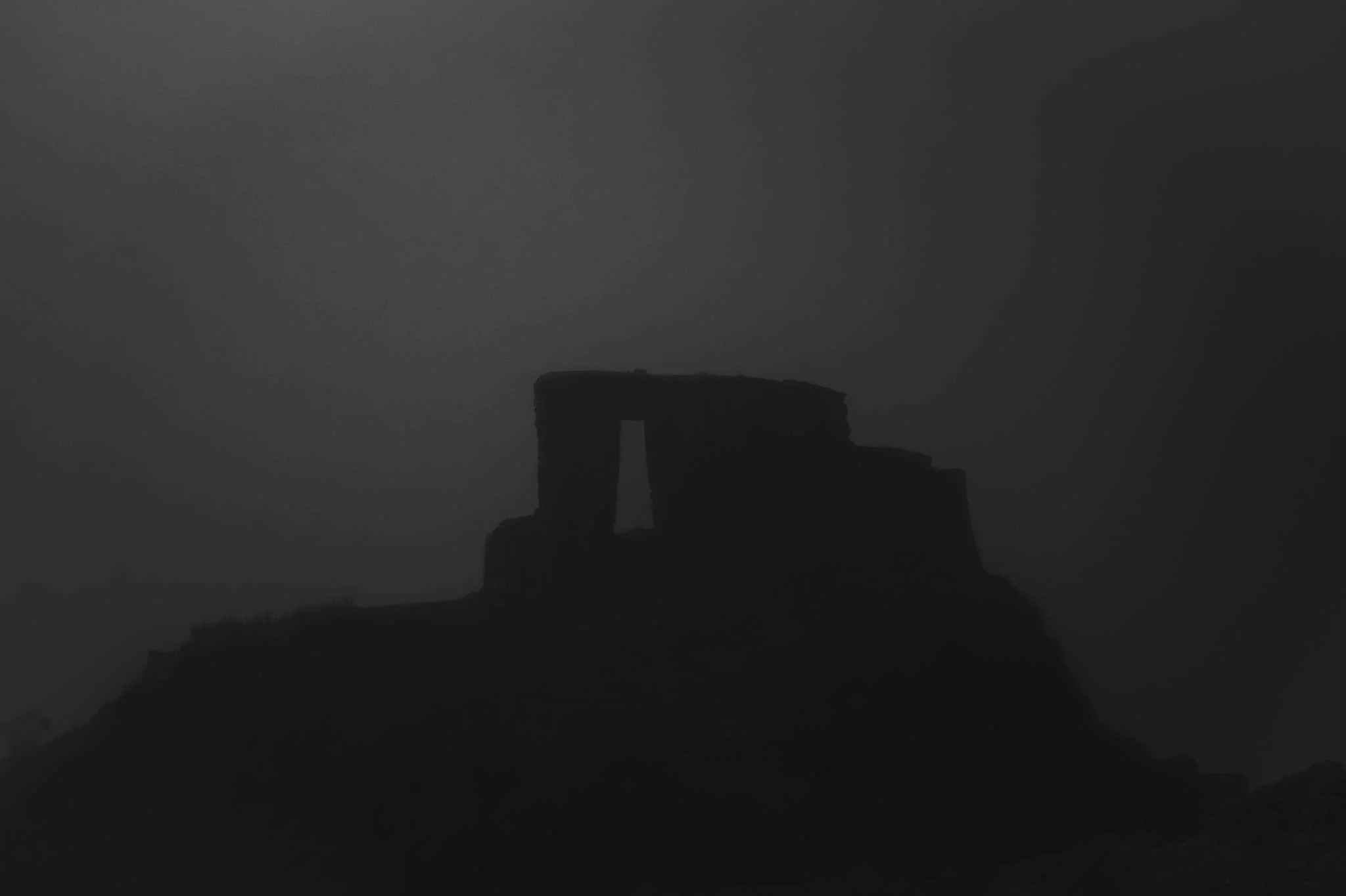 The Inti Punku ruins as a dark silhouette in thick cloud at dusk, its stone doorway just visible, Sacred Valley, Peru