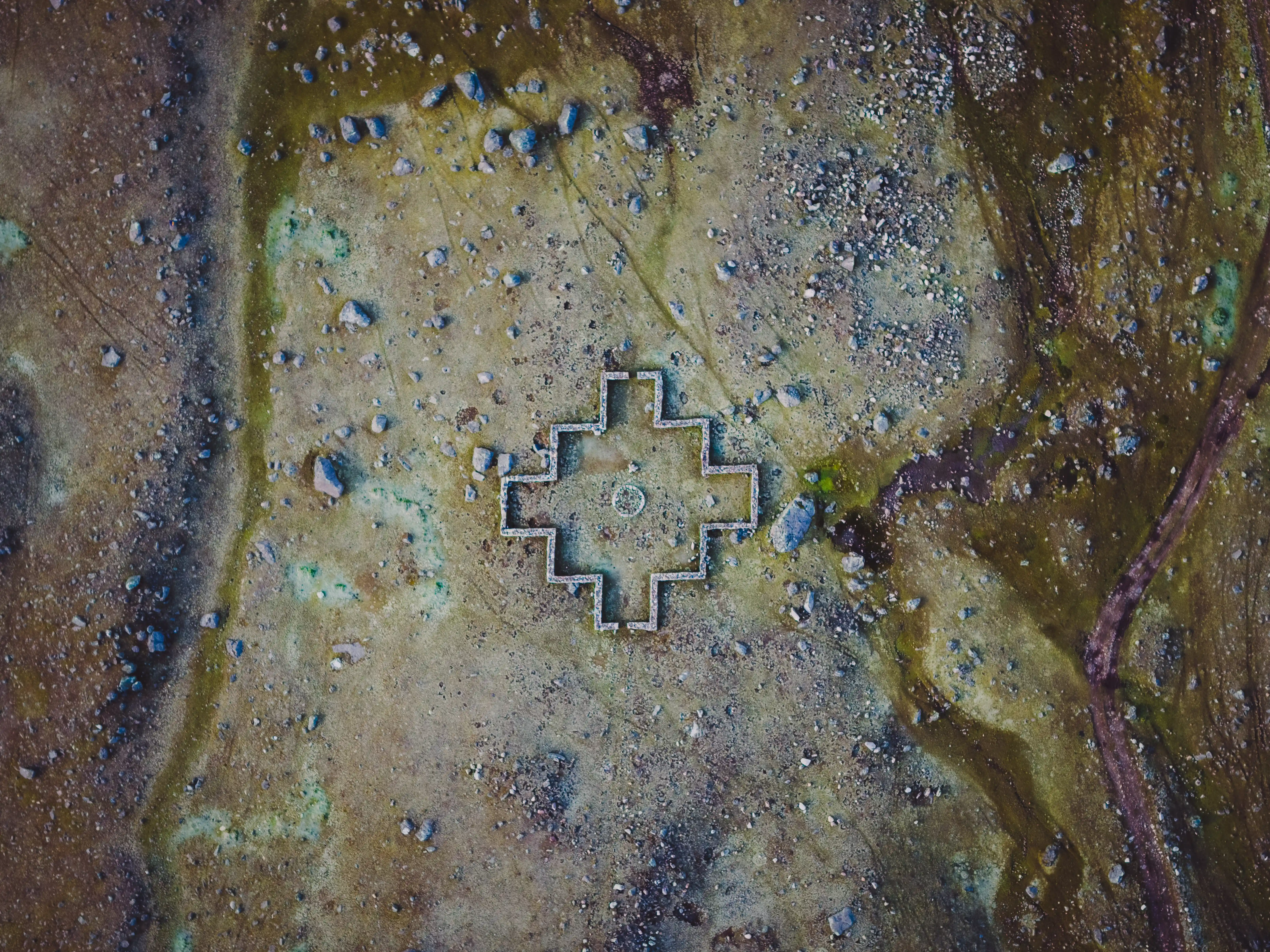 A chakana, the stepped Inca cross, carved into a weathered rock face streaked with green and ochre, Pacchanta, Peru