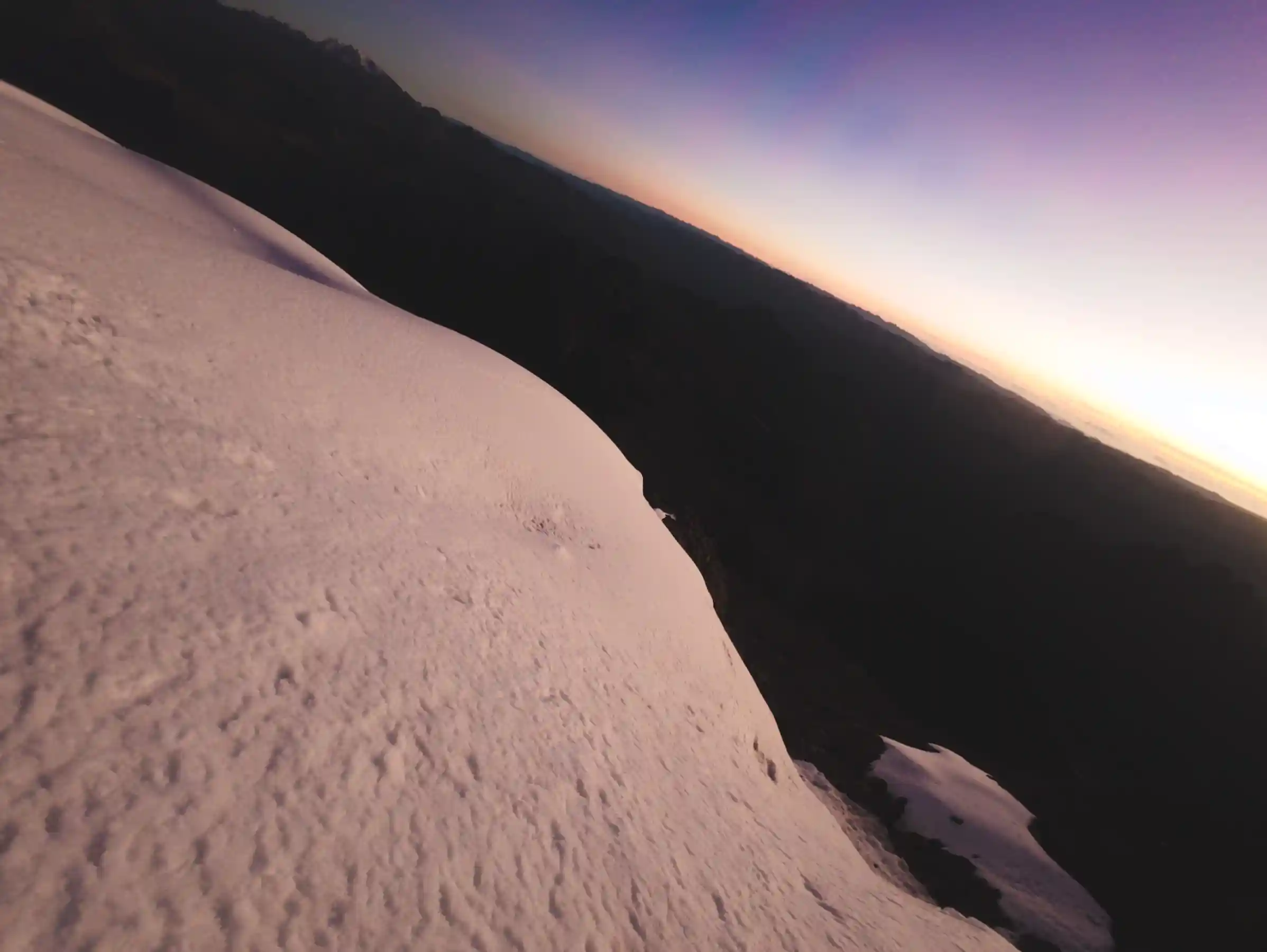 Looking down a steep snow slope at first light, the valleys towards Quiswarani and Lares still in shadow under a violet sky, Nevado Sirijuani, Peru