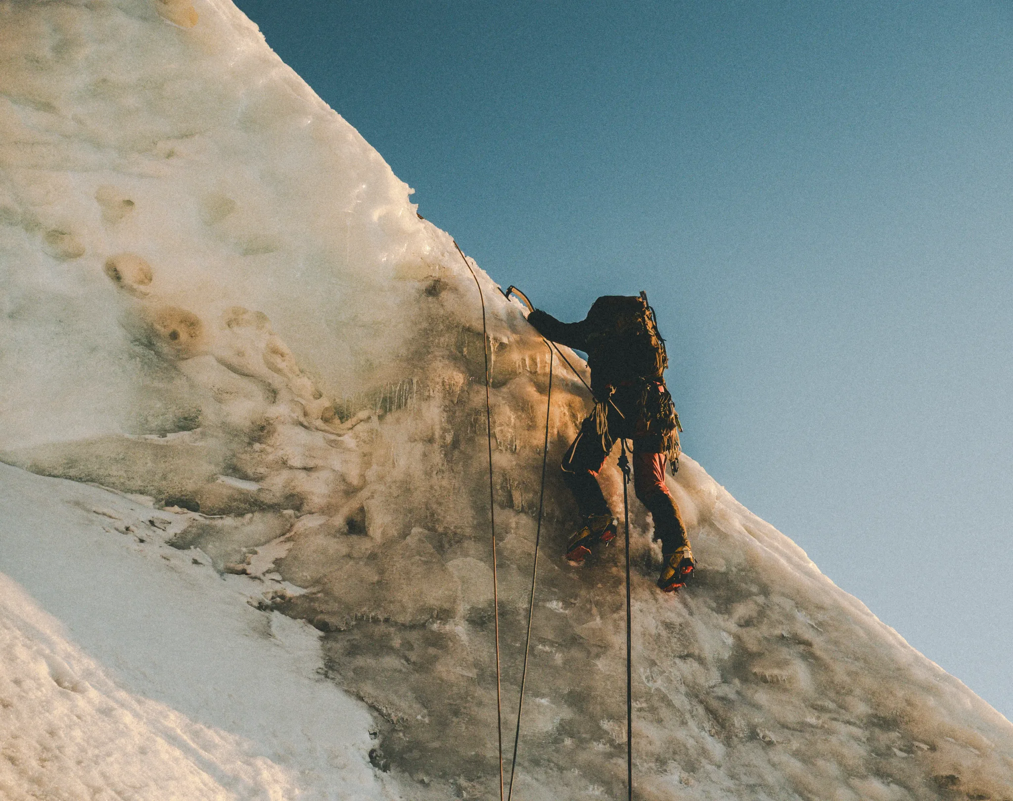 A climber leading a steep pitch of ice on the east ridge of Nevado Verónica in warm evening light, two ropes running down the face, Peru