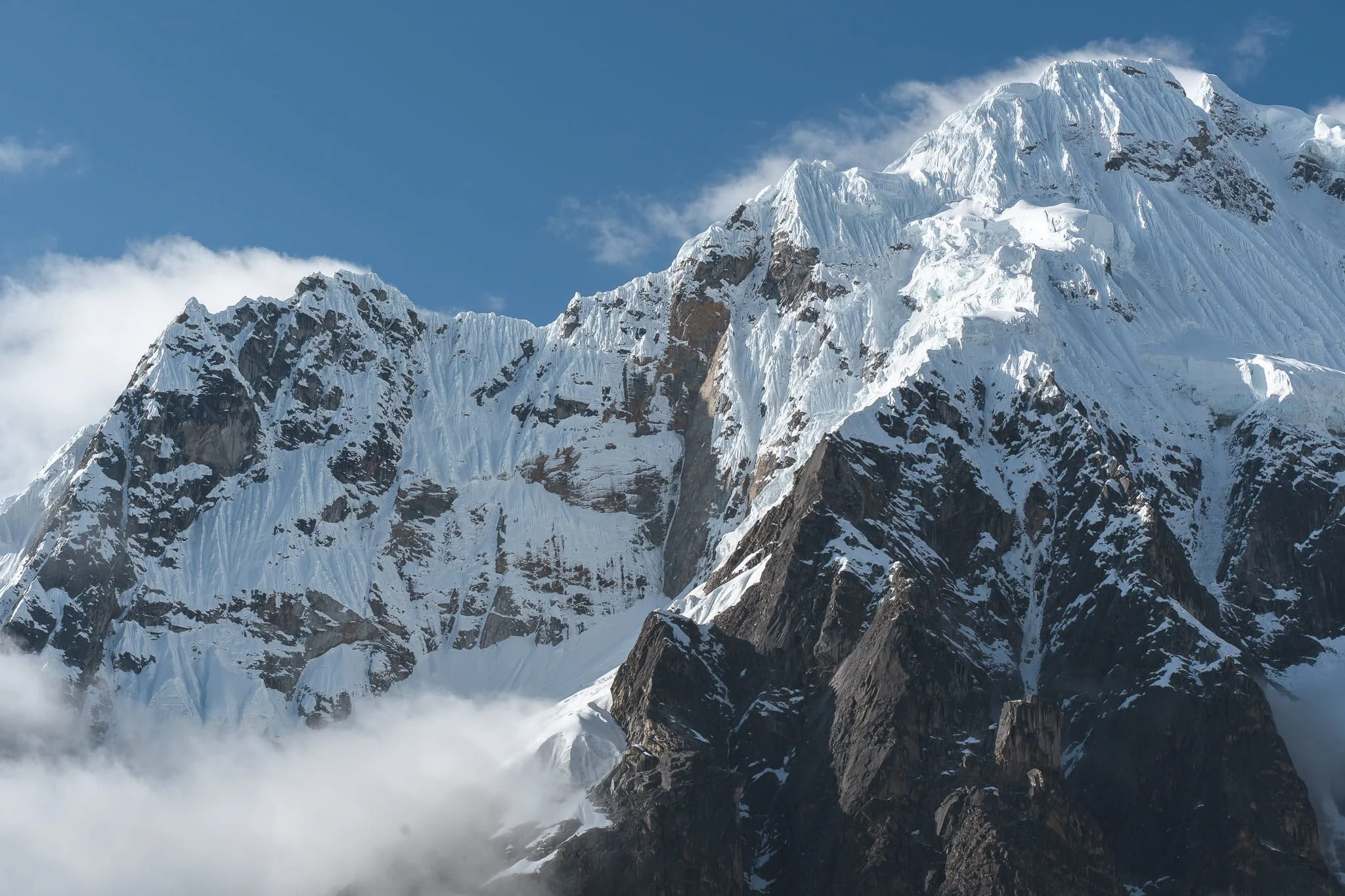 The south-west face of Salkantay, fluted with snow and ice above dark rock buttresses, cloud gathering at its base, Cordillera Vilcabamba, Peru