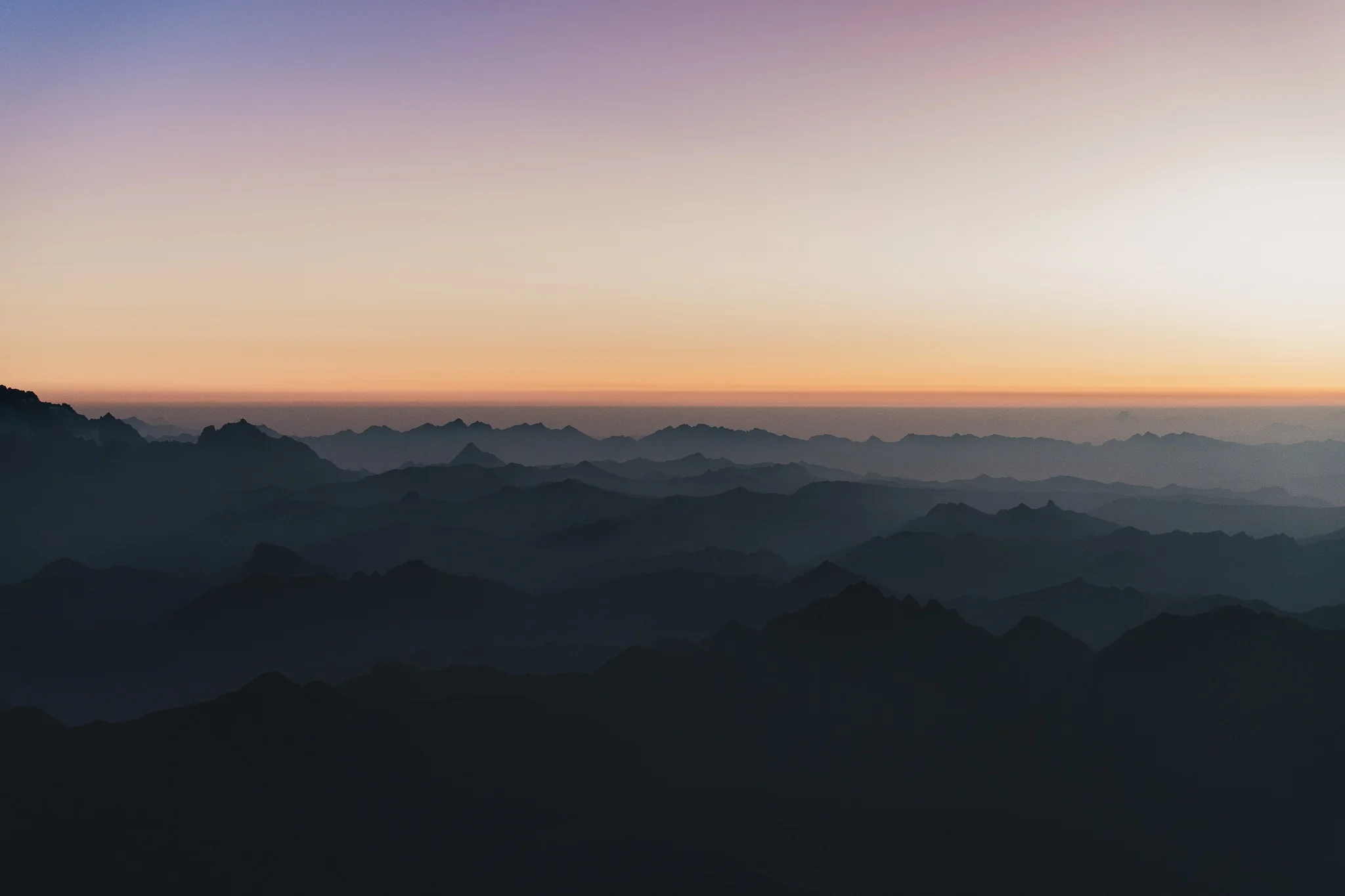 Layers of dark mountain ridges fading into haze beneath an orange and violet sky, Cordillera Urubamba, Peru
